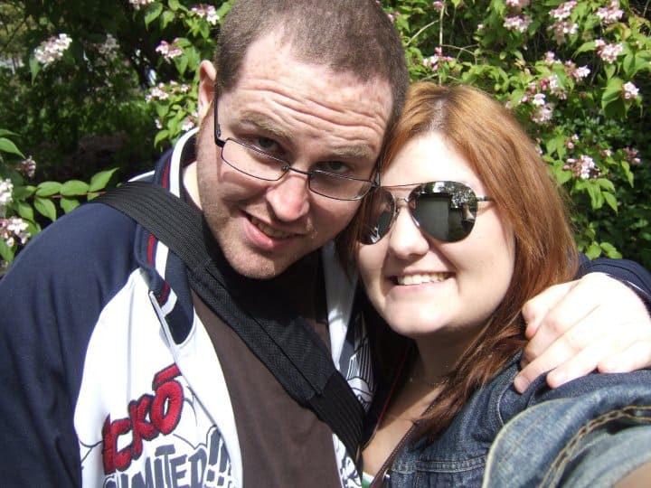 Man and a woman smiling in front of bushes