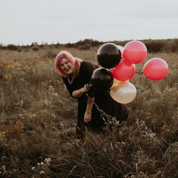 I'm laughing in a field while holding colourful balloons.